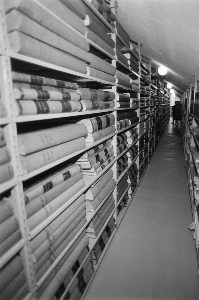 Black-and-white photo of a library asile with bookshelves on one side.