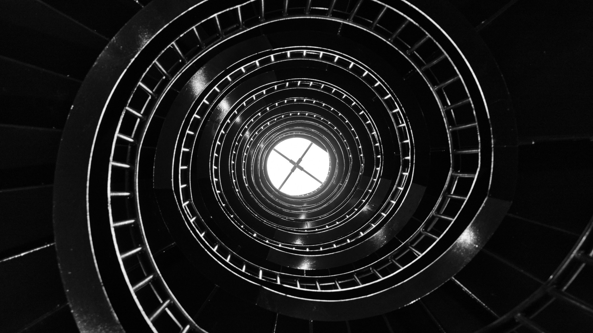 Upward view from the base of a spiral staircase through the well hole to a skylight.