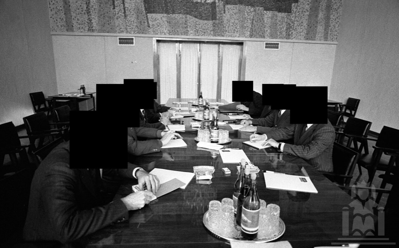 Black-and-white photo of seven figures in a summit, their faces redacted.