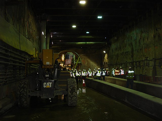 Tunnel boring machine inside a tunnel, with numerous construction workers visible.