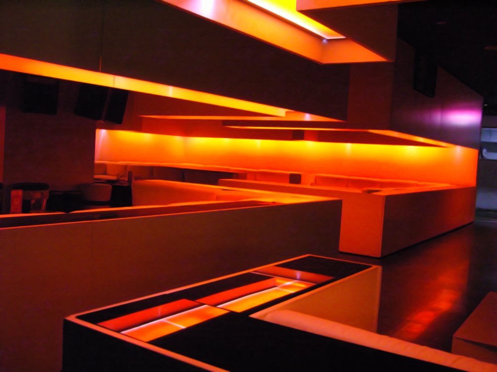 Futuristic bar interior illuminated in intense orange and purple lighting.