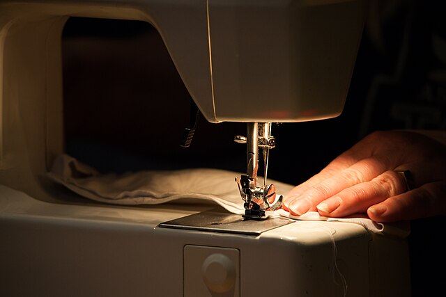 Close-up of a hand using a sewing machine to sew an object.