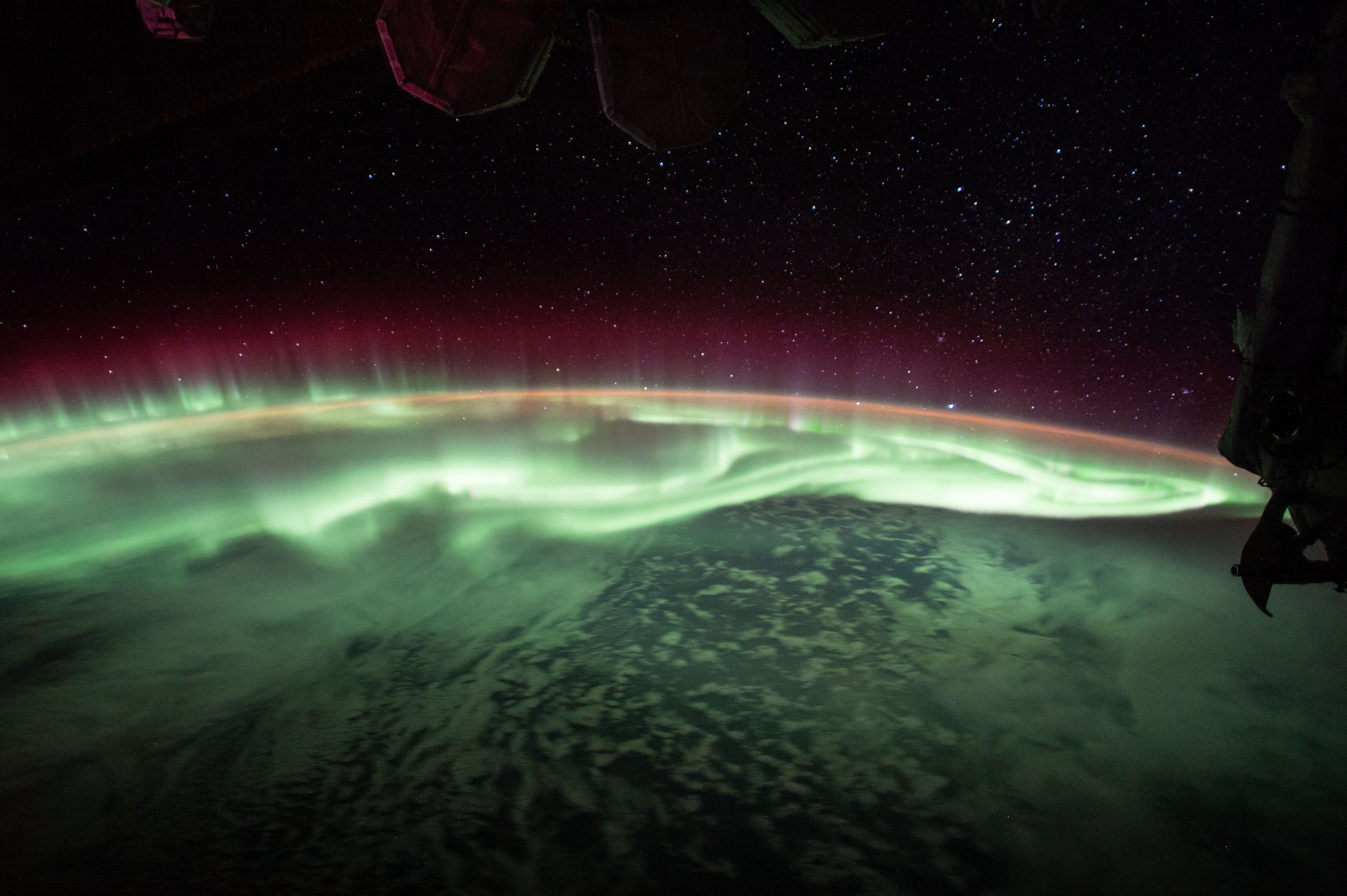 Aurora stretching over a curved planetary horizon at night, captured from outer space.